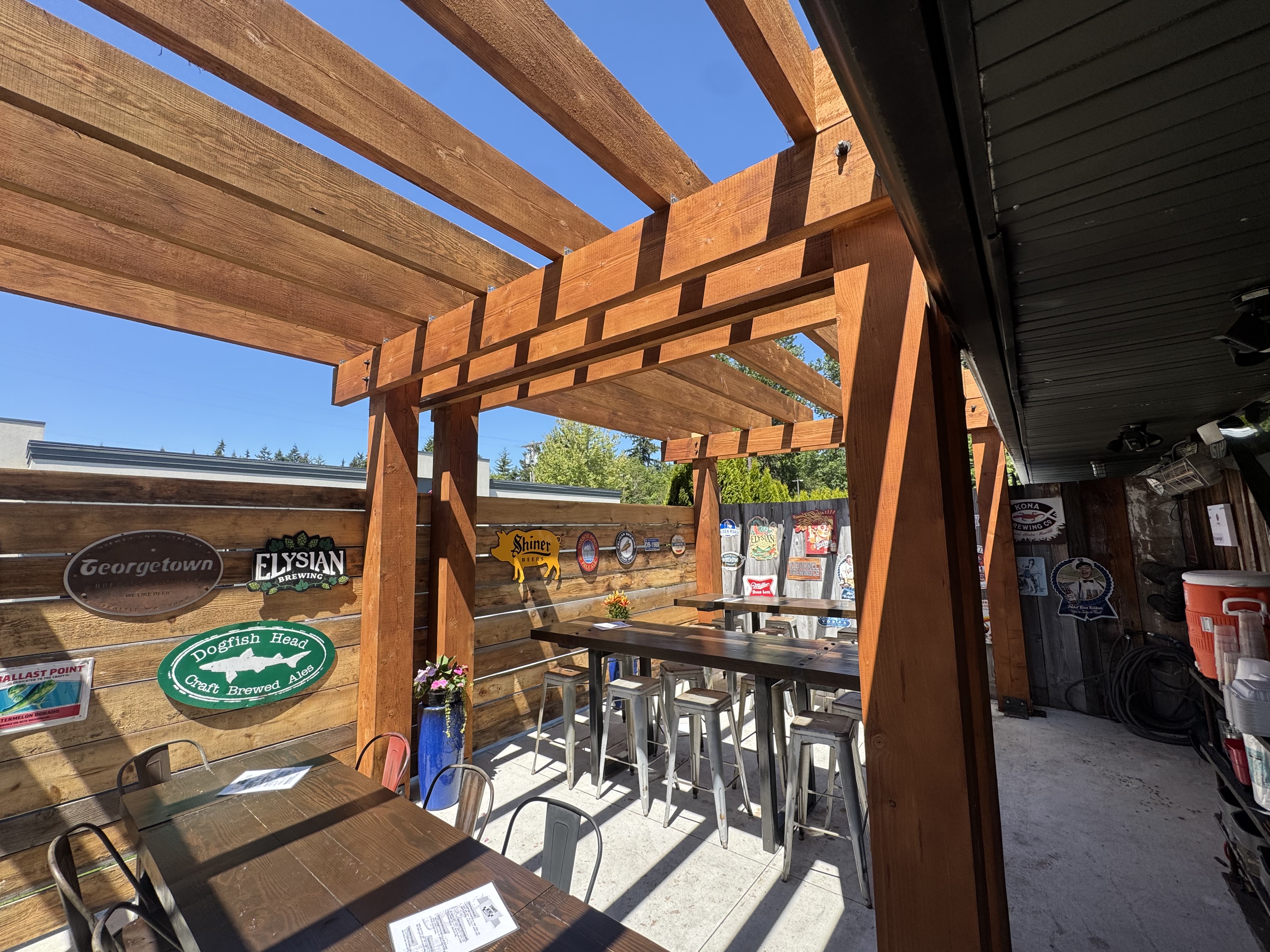 Stained timber pergola over a brewery patio with high top tables and metal stools