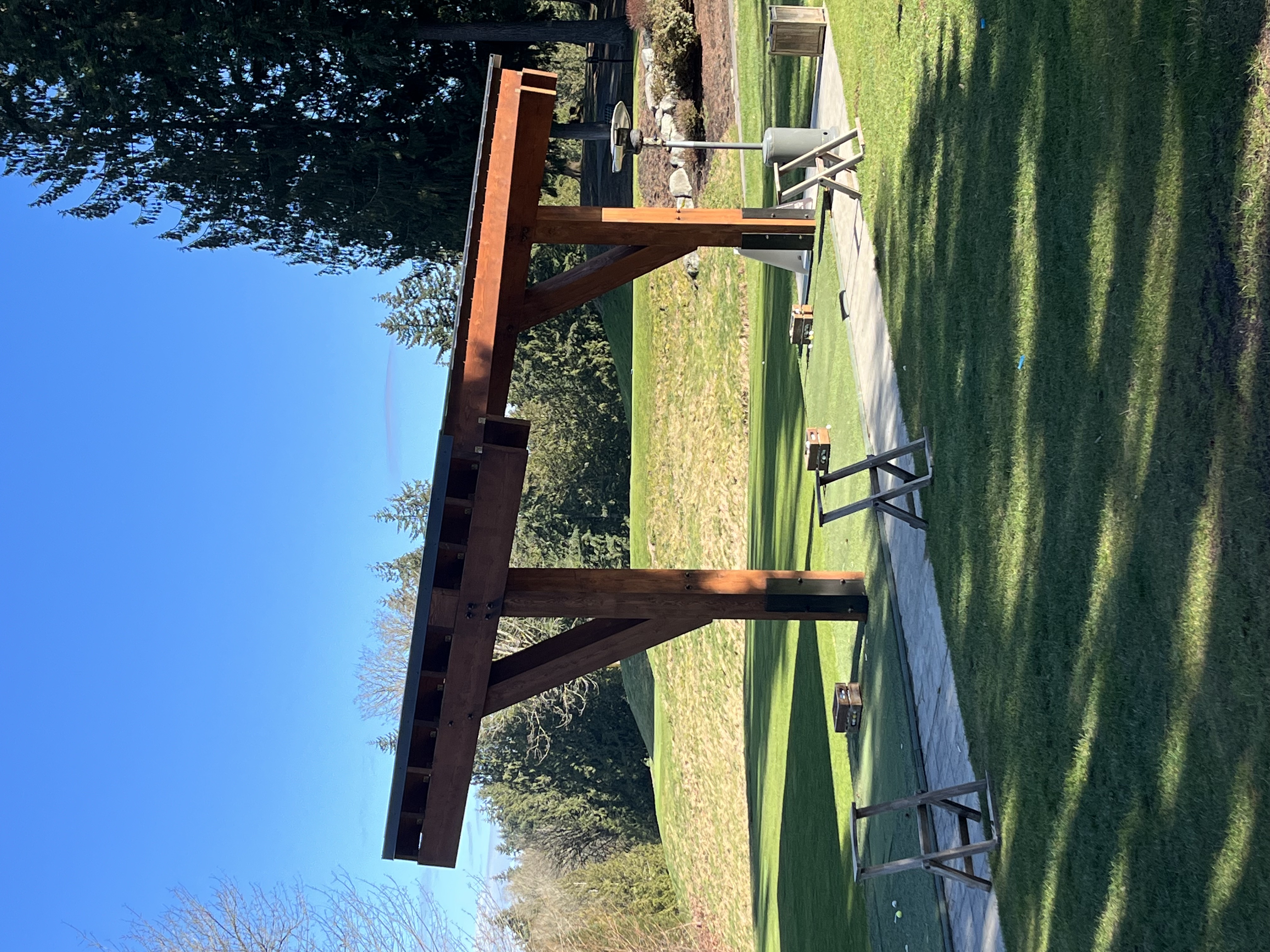 Cantilevered timber shelter with knee braces over a golf driving range tee line