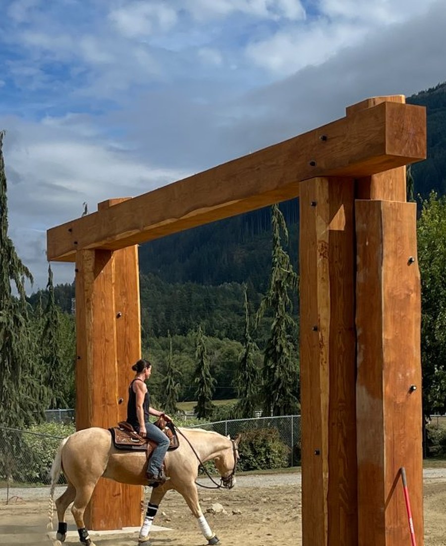 Horse and rider passing under a custom Douglas Fir timber arch entry gate, PNW mountains in background