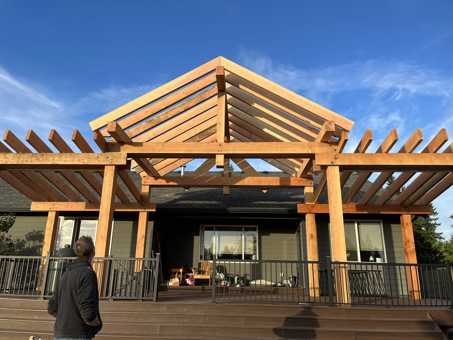 Cedar pergola and gable truss framing a covered rear deck on a home, unstained timber against blue sky
