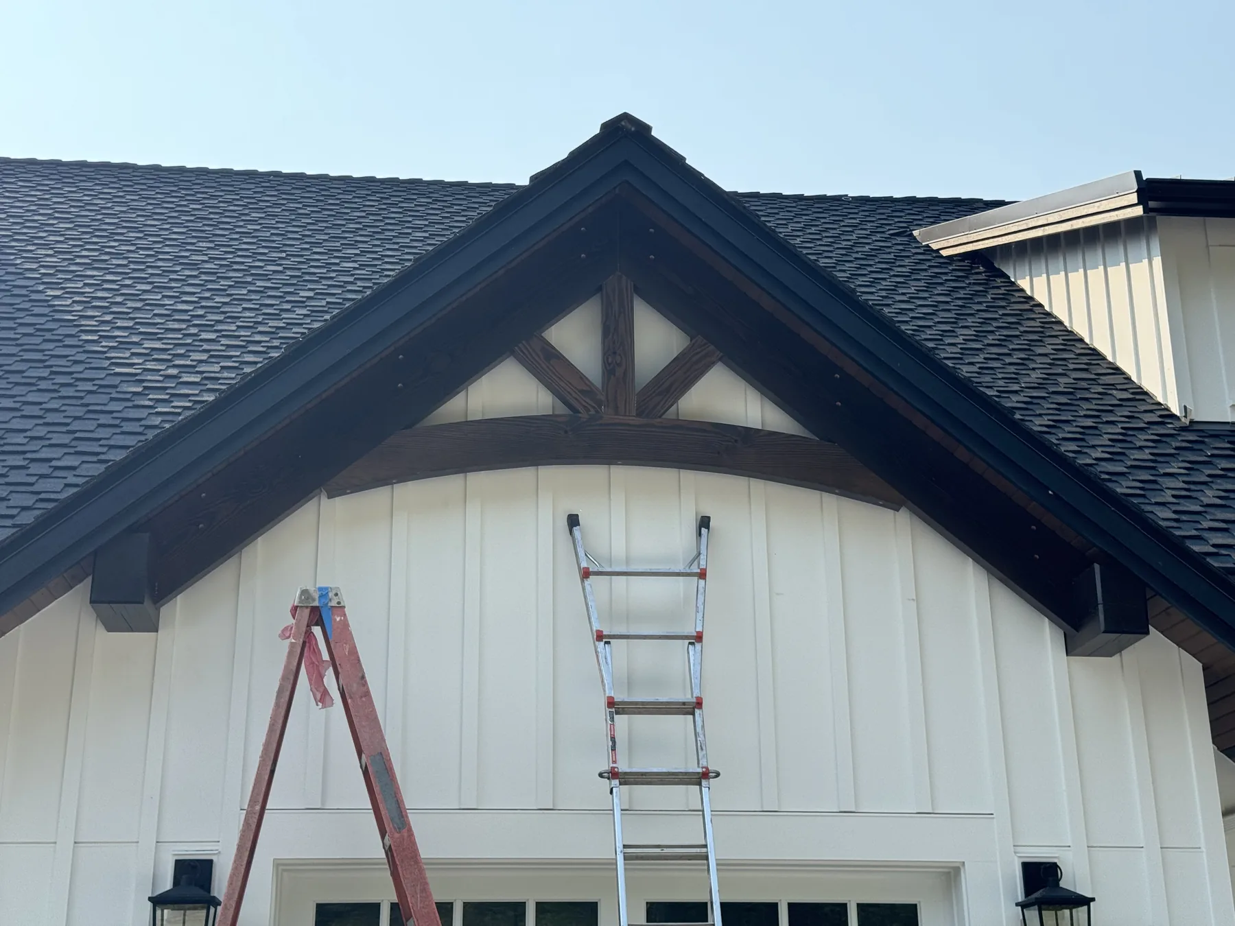 Dark stained timber gable truss set into the peak of a white board and batten farmhouse