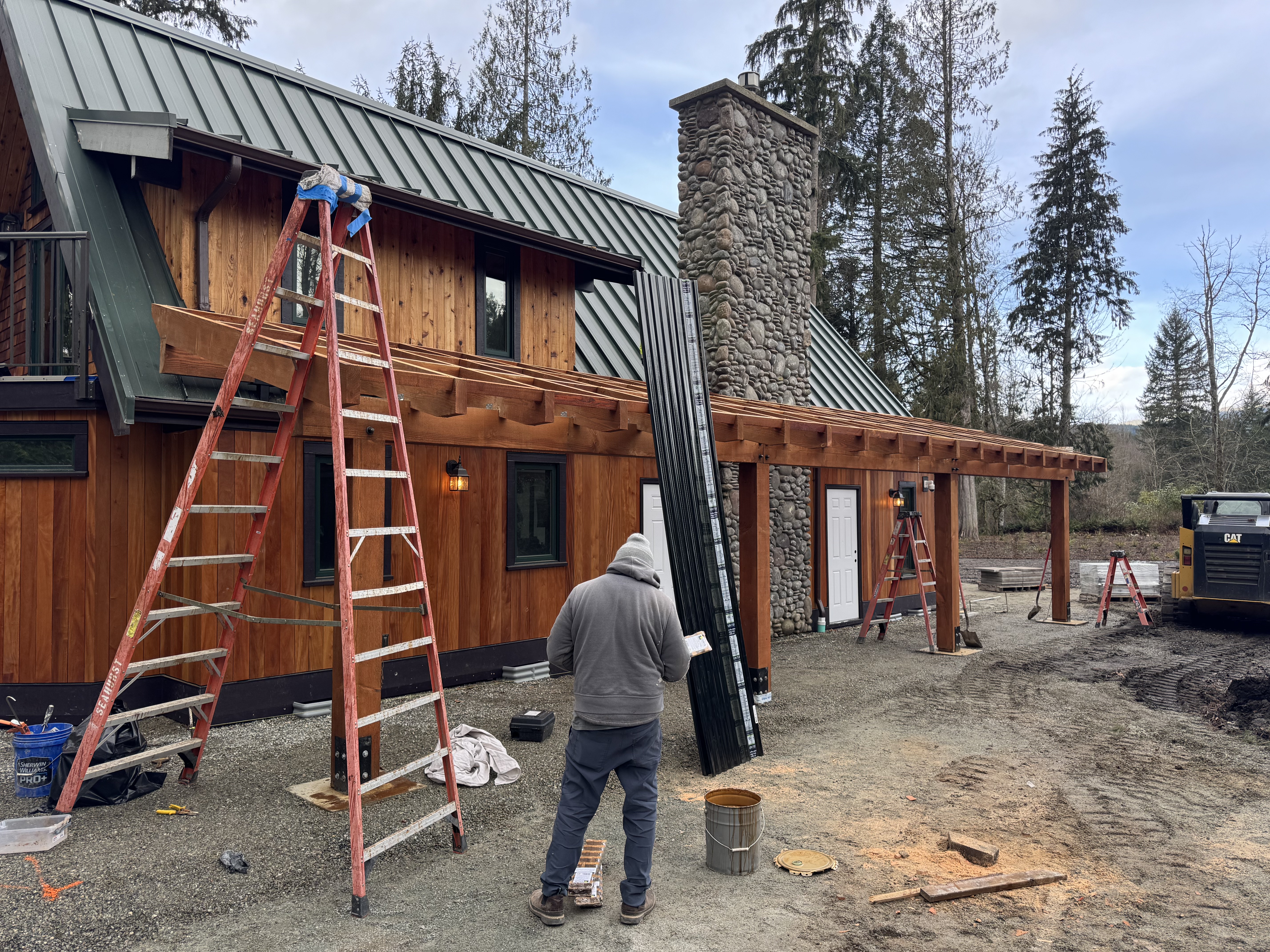 Timber porch cover going up along a cedar sided cabin with a river rock chimney and green metal roof