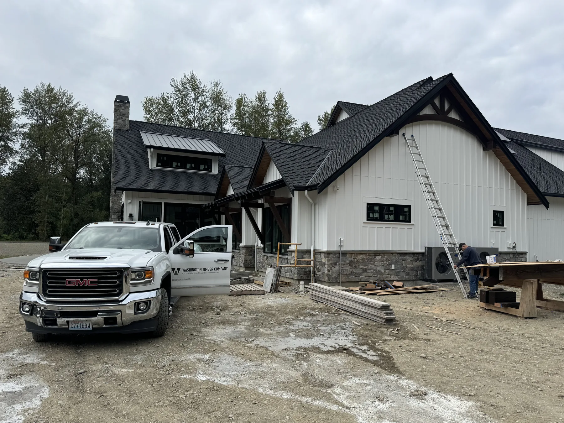 Modern farmhouse with dark stained timber entry and gable accents, Washington Timber Company truck parked on site