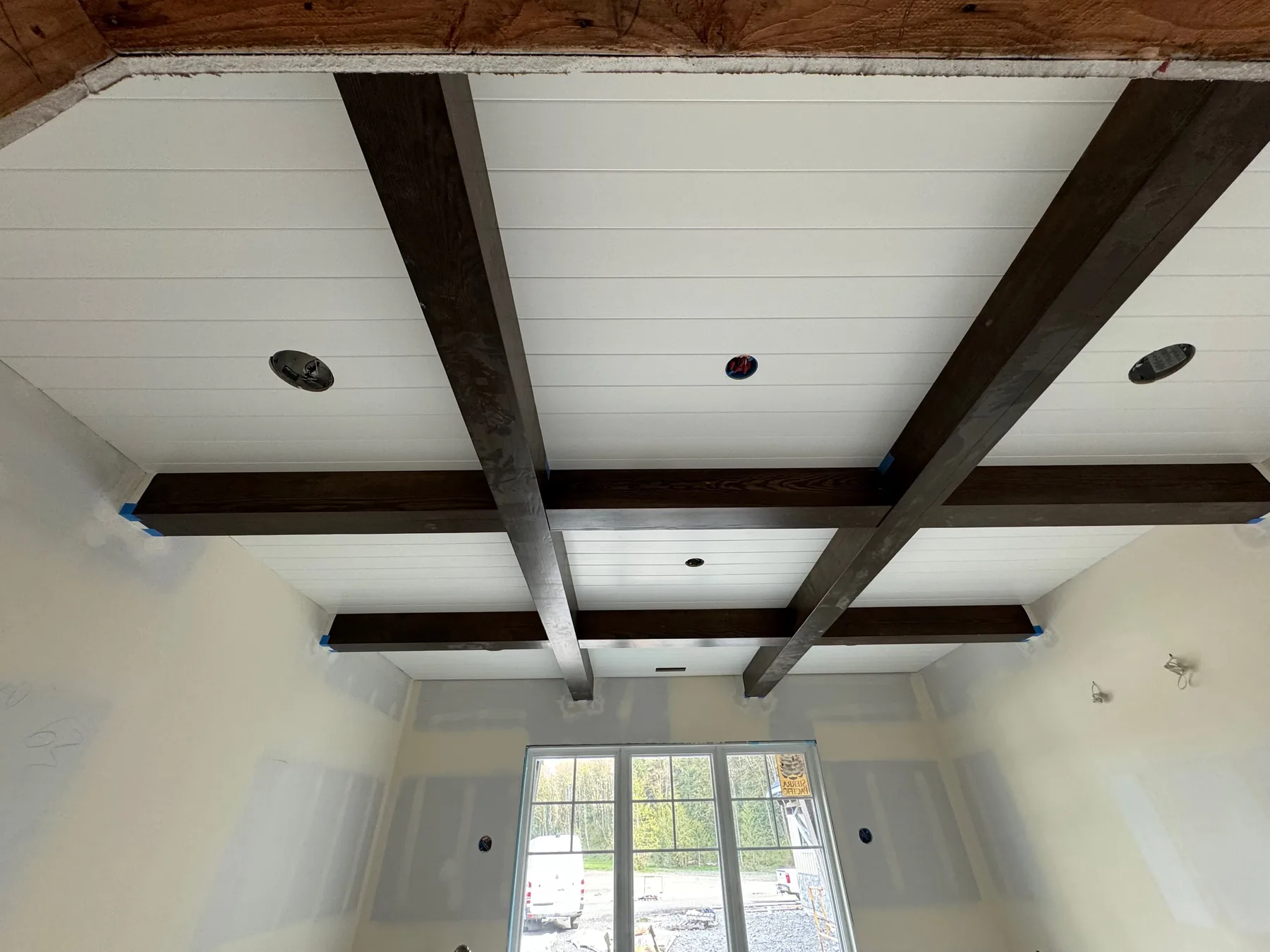 Dark stained coffered timber beam ceiling set against white shiplap in a finished room