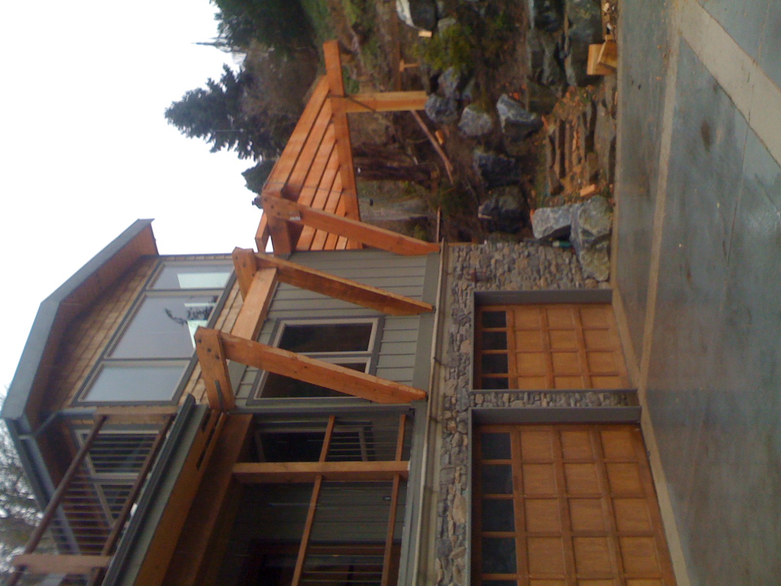 Oversized timber knee brackets and a pergola on the upper level of a hillside home above the garage