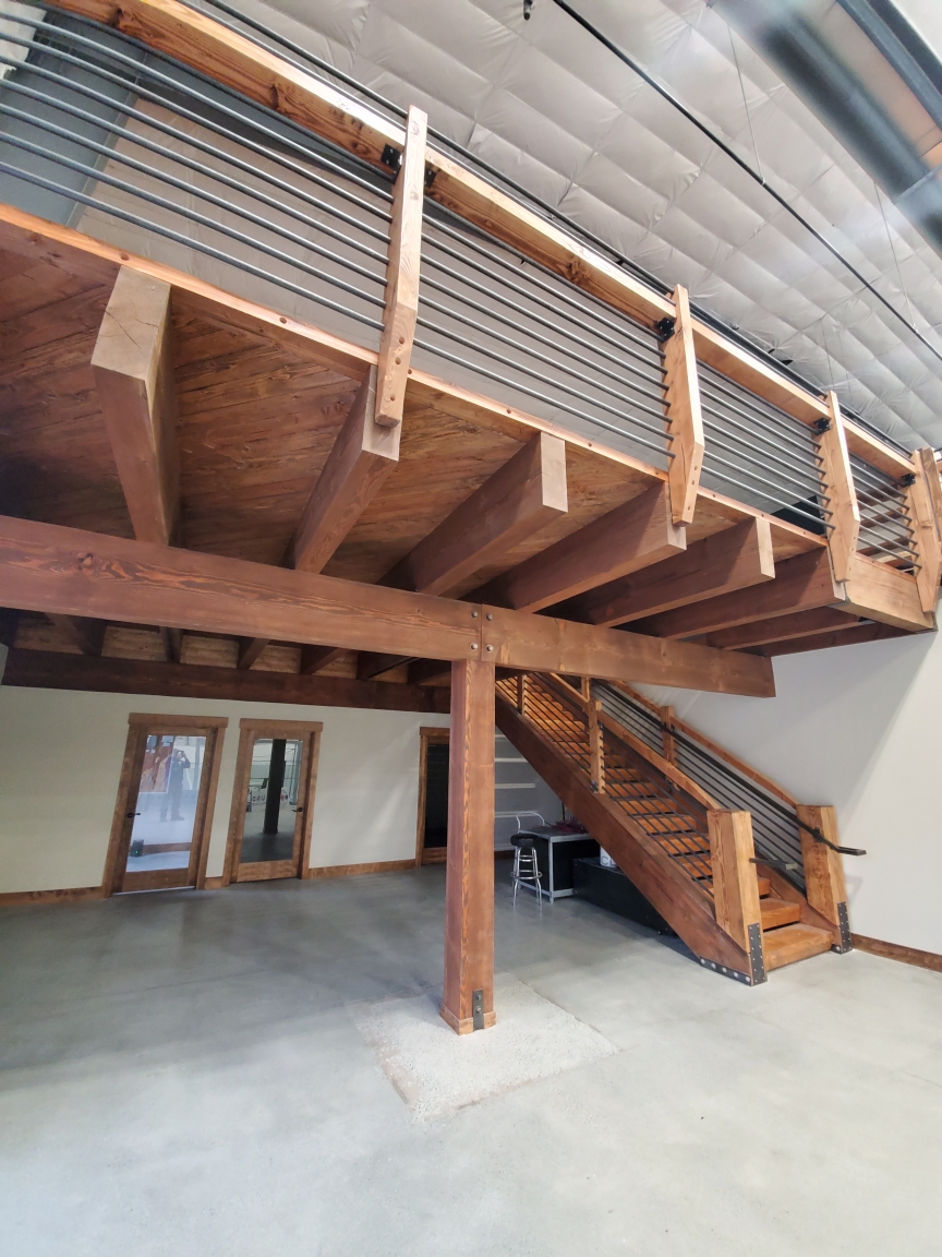 Interior timber mezzanine with heavy joists and an open stair with steel cable railing